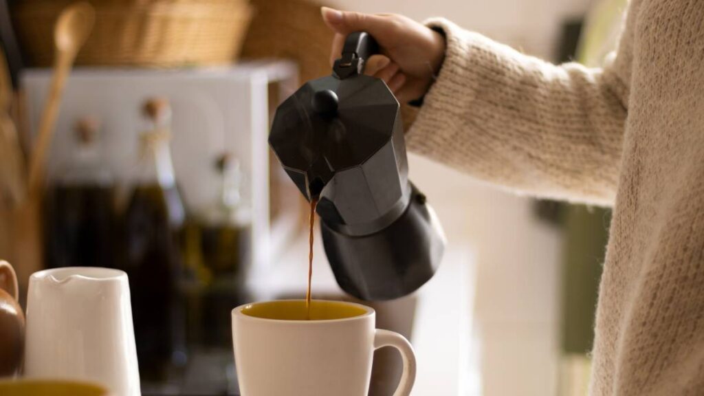 pessoa colocando café da cafeteira italiana na xícara branca