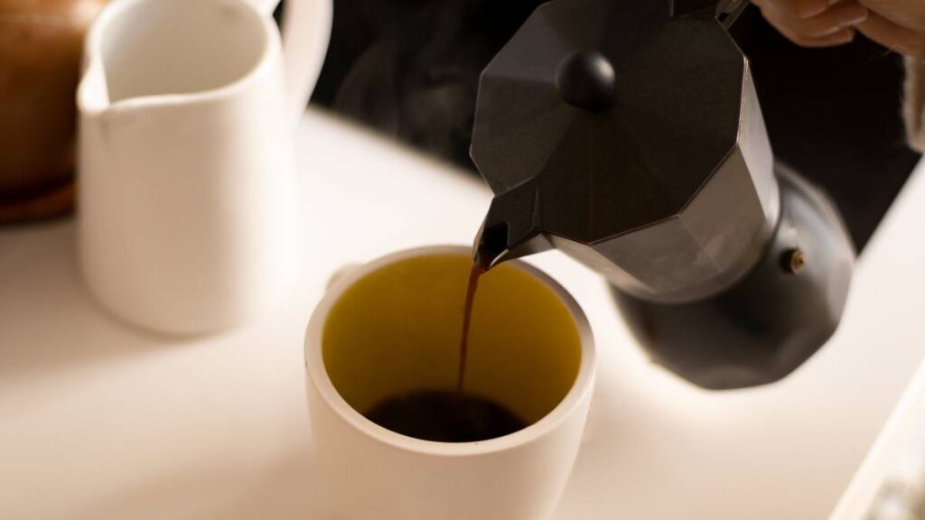 cafeteira italiana servindo café na xícara branca