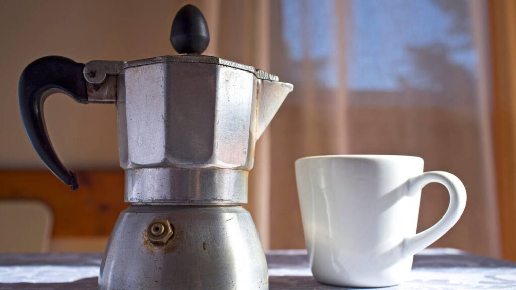 cafeteira italiana ao lado de uma xícara de café